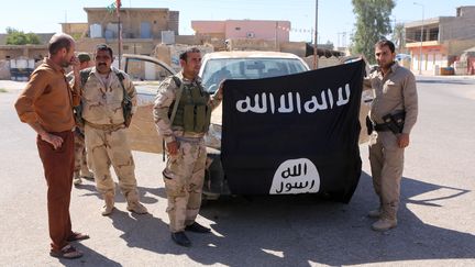 Des combattants kurdes posent avec un drapeau de l'Etat islamique dont ils se sont emparé à Makmur, en Irak, le 12 septembre 2014. (THOMAS RASSLOFF / DPA / AFP)