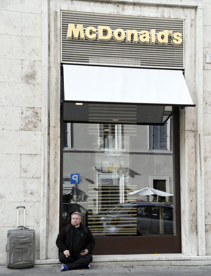 Un prêtre est assis devant le tout nouveau McDonald's proche de la place Saint-Pierre... (3 janvier 2017)
 (Tiziana Fabi / AFP)