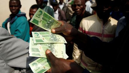 Un homme présente les nouveaux billets de 2 dollars zimbabwéens à côté de clients faisant la queue près d'une banque à Harare le 12 novembre 2019. (PHILIMON BULAWAYO / X02381)