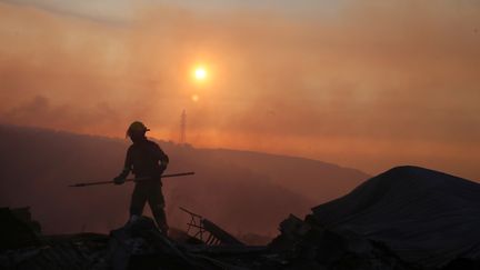 Un pompier enlève les restes des maisons détruites par le feu. (RODRIGO GARRIDO / REUTERS)