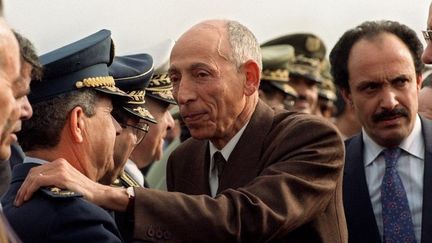 Mohamed Boudiaf (en civil au centre) salue le chef d'Etat major de l'armée, le général Abdelmalek Gueneizia (L), à l'aéroport d'Alger, le 16 janvier 1992, lors de son retour d'exil. (ABDELHAK SENNA / AFP)