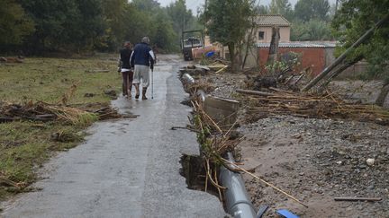 Deux personnes marchent sur une route détruite après les intempéries, le 16 octobre 2018, à Villalier (Aude). (PASCAL PAVANI / AFP)