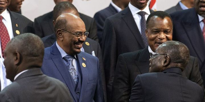 Le président soudanais Omar el-Béchir (à gauche, en costume bleu) salué par son homologue zimbabwéen Robert Mugarbe (de dos, en noir), président en exercice de l'Union africaine (UA), lors du 25e sommet de l'organisation panafricaine le 14 juin 2015. Le chef d'Etat soudanais s'est rendu en Afrique du Sud alors qu'il fait l'objet d'un mandat d'arrêt international lancé par la Cour pénale internationale (CPI). (AFP PHOTO / GIANLUIGI GUERCIA)