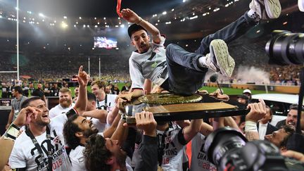 Après leur victoire en finale du Top 14, les rugbymen du Stade toulousain transportent le chanteur Oli sur le bouclier de Brennus. (ALAIN JOCARD / AFP)