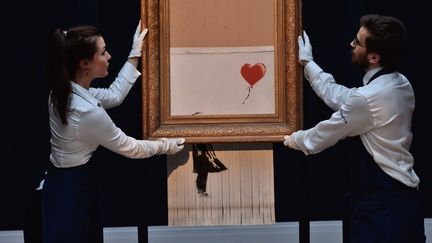 Des employés de Sotheby's dévoilent "Girl with balloon" de Banksy partiellement autodétruite et rebaptisée "Love is in the bin", le 12 octobre 2018 à Londres.
