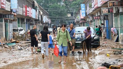 Une femme porte un sac dans une rue boueuse après les graves inondations et glissements de terrain qui ont touché ces derniers jours la ville de Gongyi, près de Zhengzhou, dans la province centrale du Henan, le 22 juillet 2021. (JADE GAO / AFP)