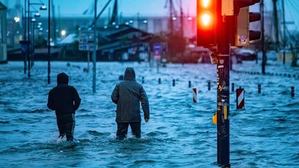 Des habitants traversent une rue inondée à Flensbourg, dans le nord de l'Allemagne, le 20 octobre 2023. (AXEL HEIMKEN / AFP)