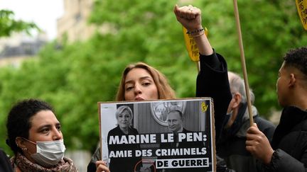 Une manifestante tient une pancarte critiquant la rencontre de Marine Le Pen et de Vladimir Poutine, en 2017, lors d'une conférence de presse de la candidate du Rassemblement national à Paris, le 13 avril 2022. (EMMANUEL DUNAND / AFP)