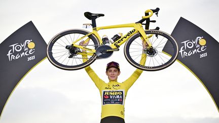 Jonas Vingegaard porte son vélo sur le podium final du Tour de France 2023, après son sacre au classement général, le 23 juillet. (MARCO BERTORELLO / AFP)