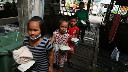 Des enfants reviennent avec leur mère d'une distribution de nourriture à Bangkok le 4 mai 2020 (ROMEO GACAD / AFP)