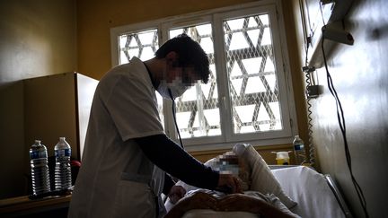 Un médecin soigne un patient détenu allongé sur un lit dans une salle de soins de l'hôpital pénitentiaire de Fresnes installé au sein de la prison, le 25 novembre 2020. (CHRISTOPHE ARCHAMBAULT / AFP)