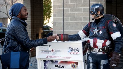 Jour de vote aux Etats-Unis. Matt Gnojek, déguisé en "Capitaine Colorado", accueille un électeur et lui donne un autocollant à l'entrée de la commission électorale de Denver, dans le Colorado (Etats-Unis), le 6 novembre 2018.&nbsp; (JASON CONNOLLY / AFP)