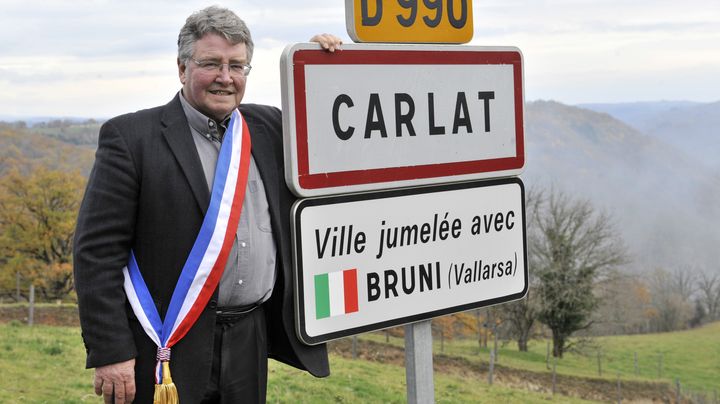 Alain Cousin, alors maire de Carlat (Cantal), pose devant le panneau d'entr&eacute;e de son village, jumel&eacute; avec Bruni (Italie), en clin d'&oelig;il &agrave; la Premi&egrave;re dame de l'&eacute;poque, le 21 novembre 2011. (THIERRY ZOCCOLAN / AFP)