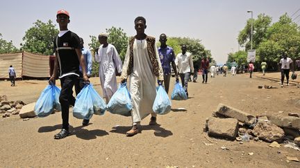 Des Soudanais portent des sacs de pain vers le sit-in devant le siège de l'armée soudanaise à Khartoum, le 5 mai 2019. (ASHRAF SHAZLY / AFP)