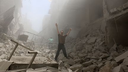 Cet homme fait des grands signes au milieu des immeubles détruits du quartier d'al-Kalasa, aux mains des rebelles, le 28 avril 2016. (AMEER ALHALBI / AFP)