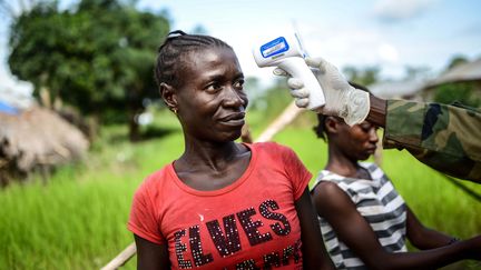 Un soldat contr&ocirc;le la temp&eacute;rature d'une femme gr&acirc;ce &agrave; un thermom&egrave;tre frontal pour d&eacute;tecter des signes de fi&egrave;vre li&eacute;s au virus Ebola, le 27 ao&ucirc;t 2014, &agrave; Nikabo (Sierra Leone). (MOHAMMED ELSHAMY / ANADOLU AGENCY / AFP)