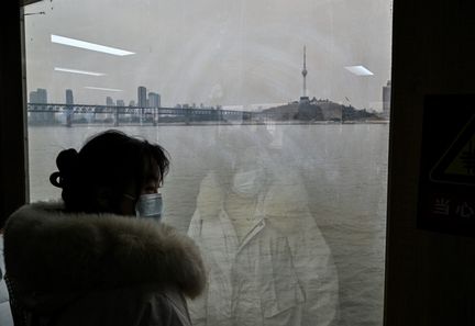 Une femme traverse le fleuve Yangtze, le 22 décembre 2024, à Wuhan (Chine), près de cinq ans après le premier mort du Covid-19 dans cette ville. (HECTOR RETAMAL / AFP)