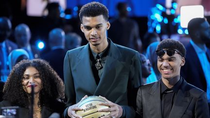 Victor Wembanyama, sélectionné par les San Antonio Spurs en première position de la draft 2023, jeudi 22 juin, à New York, entouré de sa sœur et de son frère. (JOHN MINCHILLO / AP)