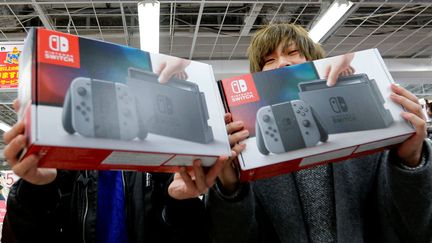 Deux Japonais posent avec leurs Switch fraîchement acquises le jour de la sortie de la nouvelle console de Nintendo à Tokyo (Japon), le 3 mars 2017. (TORU HANAI / REUTERS)