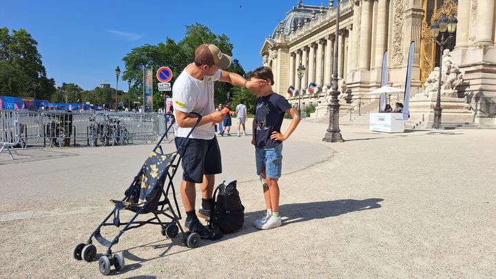 Un père tartine son fils de crème solaire devant le Grand Palais, à Paris, durant les JO, le 29 juillet 2024. (RAPHAEL GODET / FRANCEINFO)