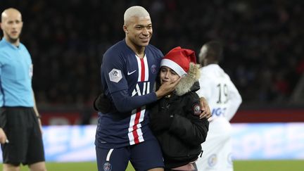 Kylian Mbappé joue au Père Noël avec un jeune garçon entré sur le terrain lors de PSG-Amiens pour faire signer son carnet, le 21 décembre 2019. (THIBAULT CAMUS/SIPA)