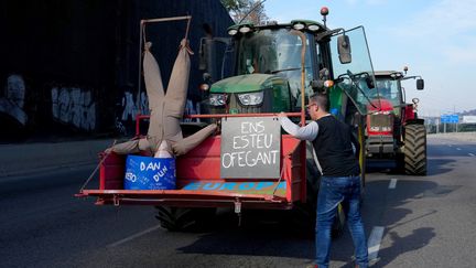 Un agriculteur espagnol manifeste, sur l'autoroute au nord de Barcelone, avec son tracteur sur lequel une pancarte indique, en catalan, "Vous nous noyez", le 7 février 2024. (PAU BARRENA / AFP)