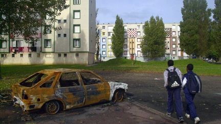 Des écoliers passent à côté d'une voiture brûlée dans le quartier de la Mare Rouge au Hâvre, novembre 2001 (AFP. M.Fedouach)