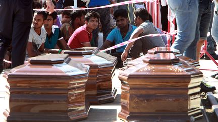 Des migrants entourent les cercueils de 13 personnes mortes en tentant de traverser la M&eacute;diterran&eacute;e, mercredi 29 juillet 2015 dans le port de Messine, en Sicile (Italie). (GIOVANNI ISOLINO / AFP)