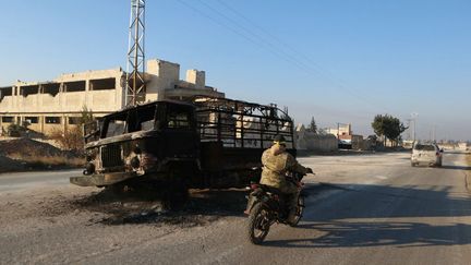 Un combattant passe en moto devant un camion incendié à Khan al-Assal, dans la province d'Alep, dans le nord de la Syrie, le 29 novembre 2024. (AAREF WATAD / AFP)