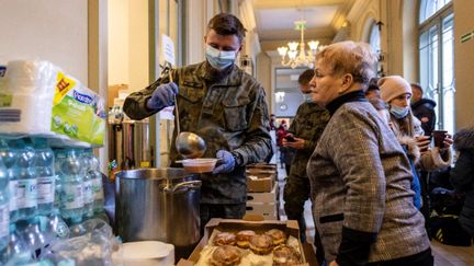 Un militaire sert de la soupe à une réfugiée ukrainienne dans une gare polonaise transformée en centre d'accueil temporaire pour les réfugiés le 25 février 2022. (Crédit Wojtek RADWANSKI / AFP)