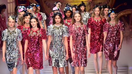 Dolce &amp; Gabbana plonge dans un joli conte de fée où tout scintille. La lueur des candélabres resplendit sur des parures strassées et vêtements chatoyants. Une robe est recouverte de fragments de miroirs dorés, un manteau en or est parsemé de minuscules fils en lurex, tout comme des robes dans des tons rose ou bleu. Ça, c'est pour le côté princesse. Côté Cendrillon, les robes sont plus simples, en flanelle de laine noire. De petits traits blancs y dessinent bords et structure du vêtement à la manière des coups de craie ou des coutures en fil à bâtir utilisés par les couturières sur leur patron. Le prince charmant est de la partie avec manteaux queue de pie, vestes de Hussard aux brandebourgs dorés et pantalons à galon rouge. Ici et là, des motifs brodés ou imprimés rappellent le monde enchanté des fables, tels que souris, chats, oiseaux, lustres, bougies et clés dorées. La plupart des tenues sont associées à une collerette amovible en dentelles et perles, tandis qu'un ruban recouvert de pierres précieuses, noué sur la tête, joue les diadèmes.
 (GIUSEPPE CACACE / AFP)