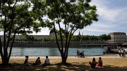 A Lyon, des habitants assis sur la pelouse sèche des quais de la ville, lors d'une vague de chaleur, le 18 mai 2022. (OLIVIER CHASSIGNOLE / AFP)