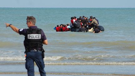 Un policier face à une embarcation de migrants tentant la traversée de la Manche depuis une plage de Sangatte, dans le Pas-de-Calais, le 18 juillet 2023. (BERNARD BARRON / AFP)