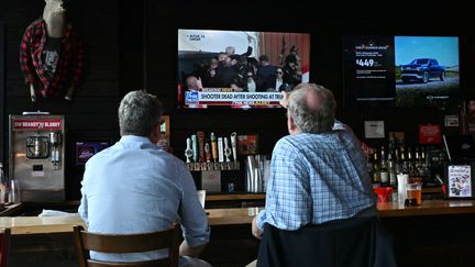 Deux Américains suivent des informations concernant la tentative d'assassinat de Donald Trump à la télévision, dans un bar à Milwaukee, dans le Wisconsin (Etats-Unis), le 13 juillet 2024. (ANGELA WEISS / AFP)