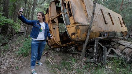 Une touriste se photographie devant un autobus abandonné, lors d'une visite à Tchernobyl (Ukraine), le 7 juin 2019. (MAXPPP)