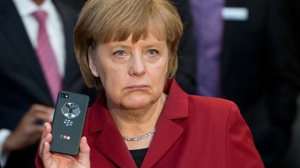 La chanceli&egrave;re allemande, Angela Merkel, brandit un t&eacute;l&eacute;phone prot&eacute;g&eacute; contre les &eacute;coutes t&eacute;l&eacute;phoniques, lors d'un salon &agrave; Hanovre (Allemagne), le 5 mars 2013. (JULIAN STRATENSCHULTE / DPA / AFP)