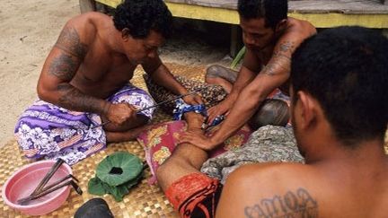 Tiatia Tafili Faitele, l'un des neuf tatoueurs de l'île de Savaii (Samoa), officie sur la cheville du jeune Avea (DOZIER Marc)