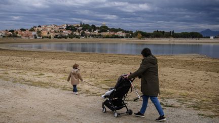 Des passants se promènent au bord du lac, sec pour la saison, de Villeneuve-de-la-Raho (Pyrénées-Orientales), le 13 décembre 2023. (ED JONES / AFP)