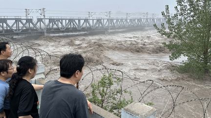 Les résidents locaux regardent une rivière en crue dans la banlieue de Pékin, le 1ᵉʳ août 2023. (ICHIRO OHARA / YOMIURI / AFP)