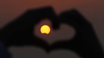 Une personne fait un coeur avec ses doigts, en 2013, au Koweit, lors d'une éclipse&nbsp;partielle du soleil. (YASSER AL-ZAYYAT / AFP)