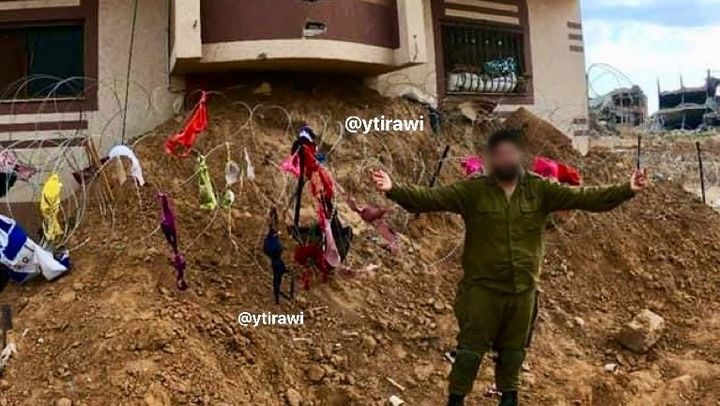 Un soldat israélien pose devant des barbelés à Gaza, auxquels sont suspendus des soutien-gorge de femmes palestiniennes. (X / YOUNIS TIRAWI)