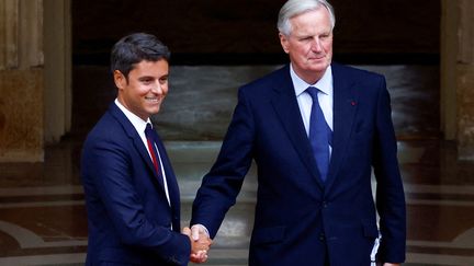 Michel Barnier serre la main de Gabriel Attal, lors de la cérémonie de passation de pouvoir à l'hôtel Matignon, à Paris, le 5 septembre 2024. (SARAH MEYSSONNIER / AFP)