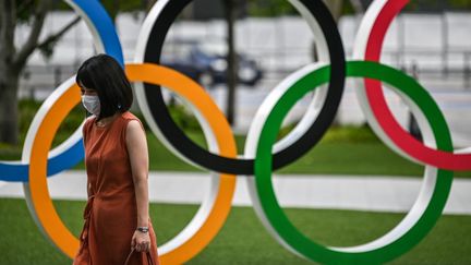 Une femme portant un masque devant les anneaux olympiques à Tokyo, le 24 août 2020. (CHARLY TRIBALLEAU / AFP)