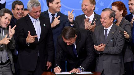 Le président brésilien Jair Bolsonaro signe le décret qui facilite la possession, le port et l'importation d'armes lors d'une cérémonie au Palais Planalto, le 7 mai 2019. (EVARISTO SA / AFP)