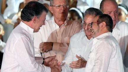 Le président colombien, Juan Manuel Santos (à gauche), salue le chef des Farc,&nbsp;Rodrigo Londoño, et le président cubain Raul Castro (à droite) lors de la signature de l'accord de paix. (LUIS ACOSTA / AFP)