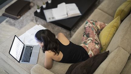 Une femme en pyjama en plein télétravail sur son canapé. Photo d'illustration. (CAIA IMAGE/SCIENCE PHOTO LIBRARY / NEW)