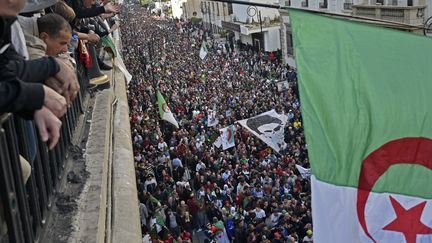 Des Algériens brandissent un drapeau national alors qu'ils regardent des manifestants anti-gouvernementaux défiler dans la capitale Alger, le 6 décembre 2019. (RYAD KRAMDI / AFP)