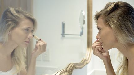 Une femme se maquille face à un miroir. (MAXPPP)