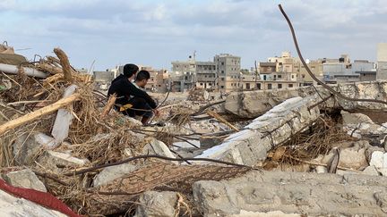 Des gens sont assis parmi les décombres de la ville de Derna, en Libye, le 20 septembre 2023. (ABU BAKR AL-SOUSSI / AFP)