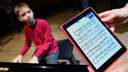 Un jeune pianiste interprète une partition affichée sur une tablette numérique. (ATTILA KISBENEDEK / AFP)